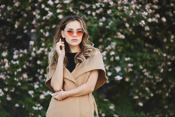 Chica modelo rubia de moda y sensual con abrigo sin mangas y gafas de sol con estilo —  Fotos de Stock