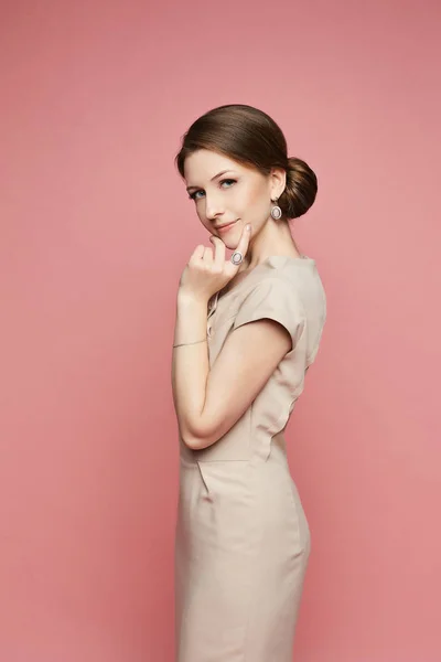 Menina modelo morena bonita e elegante em um vestido bege com jóias elegantes isoladas em fundo rosa — Fotografia de Stock