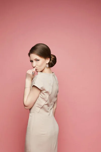 Эмоциональная брюнетка модель девушка в бежевом платье со стильными украшениями изолированы на розовом фоне — стоковое фото