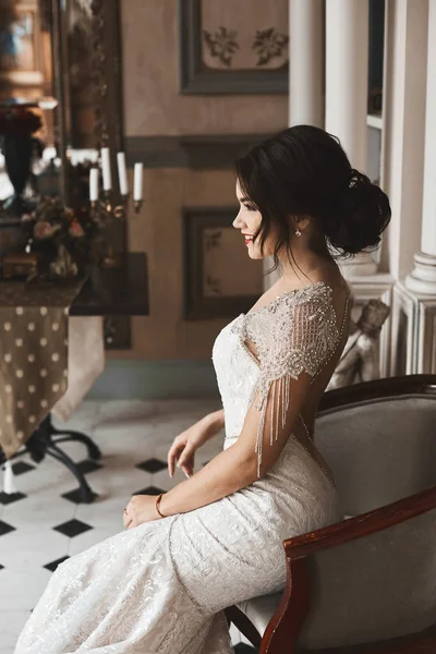 Belle, sexy et à la mode fille modèle brunette avec maquillage lumineux et coiffure élégante, dans la robe de dentelle de luxe souriant et posant à l'intérieur vintage — Photo