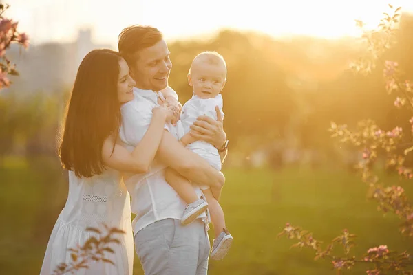 Belos pais jovens e seu filho pequeno bonito abraçando e sorrindo ao pôr do sol — Fotografia de Stock