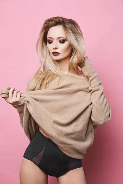 Sexy and sensual blonde model girl with blue eyes, perfect body and bright makeup, in black stylish lingerie and fasionable sweatshirt posing at pink background — 图库照片