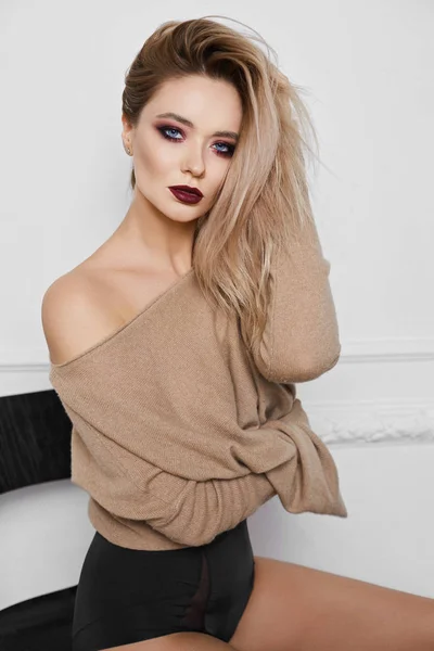 Porträtt av sexiga och vackra blond modell flicka med ljus makeup och fantastiska blå ögon svarta snygga underkläder och tröja sitter på en stol och poserar på rosa bakgrund — Stockfoto