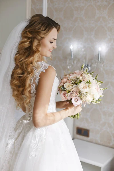 Beautiful young blonde bride with stylish wedding hairstyle in a white fashionable dress with a bouquet of flowers in her hands — Stock Photo, Image