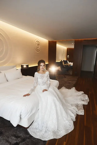 Elegant and beautiful young bride in lace dress posing on the bed at the luxury interior — Stock Photo, Image