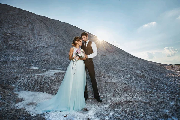 Fashionable and beautiful couple, happy blonde model girl with stylish hairstyle, in a white lace dress and stylish handsome man in the trendy suit on the salt mountain — Stock Photo, Image