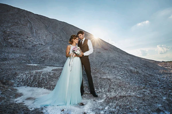 Pareja de moda y hermosa, modelo rubia feliz chica con peinado elegante, en un vestido de encaje blanco y un hombre guapo con estilo en el traje de moda en la montaña de sal —  Fotos de Stock