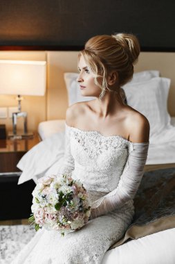 Elinde çiçekler bir buket ile bir düğün dantel elbise güzel sarışın model kız yatakta oturur ve şık lüks iç poz