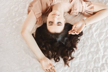 Güzel ve şehvetli esmer model kız nazik makyaj ile ve bej elbise mükemmel bir cilt ile Vintage iç yatakta poz, üst görünüm