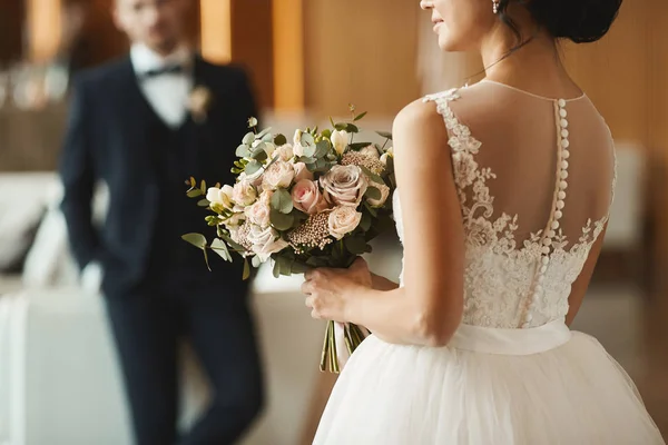 Couple à la mode, beau jeune homme dans le costume élégant et belle fille modèle brune avec coiffure de mariage en dentelle blanche robe tenant un bouquet de fleurs — Photo