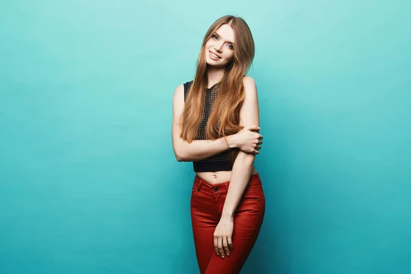 Glückliches und schönes blondes Model-Mädchen mit perfektem Körper in schwarzem stylischem T-Shirt und roter Hose, die vor blauem Hintergrund posiert, isoliert — Stockfoto