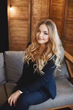 Şık bir koyu mavi elbise mavi gözleri ile güzel ve şık genç sarışın iş Bayan bir kanepede oturur ve Loft iç poz