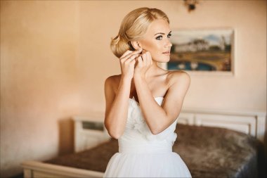 Güzel ve şık genç gelin, mavi gözleri ve küpesini ayarlama ve iç, düğün hazırlık sabah poz beyaz elbiseli şık saç modeli ile seksi sarışın model kız