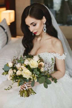 Parlak makyaj ile güzel ve Busty esmer model kız ve elinde çiçekler büyük bir buket tutan bir moda gelinlik elmas ile lüks büyük küpe ile