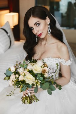 Parlak makyaj ile güzel ve Busty esmer model kız ve elinde çiçekler büyük bir buket tutan bir moda gelinlik elmas ile lüks büyük küpe ile