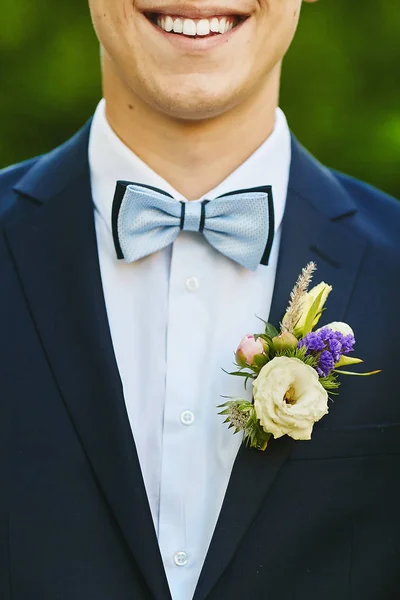 Joven elegante y guapo con la hermosa sonrisa brillante en un traje azul con corbata de moda y boutonniere colorido detalles de la boda — Foto de Stock