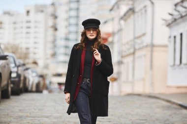 Güzel ve şık kız, şapka, palto ve güneş gözlüğü, sokakta yürüyüş