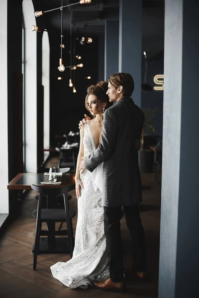 Fashionable and beautiful couple, sexy and elegant brunette model girl with bright make-up and stylish hairstyle in silver dress and stylish handsome men in trendy coat posing at restaurant interior