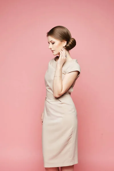 Modelo morena na moda, mulher bonita com penteado elegante em vestido bege moderno posando com olhos fechados em fundo rosa — Fotografia de Stock