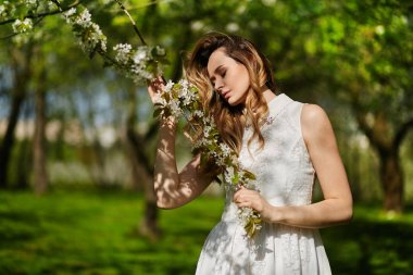 Parkta açık havada poz veren beyaz elbiseli güzel ve şık genç sarışın kadın