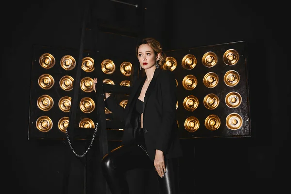 Linda, sexy, elegante menina loira semi-nua em uma jaqueta preta e leggings posando com lâmpadas de estúdio em um fundo — Fotografia de Stock
