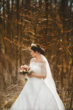 Parlak makyaj ve açık havada çiçek bir buket ile şık bir gelinlik kafasına çiçek çelenk ile zarif ve genç esmer kadın