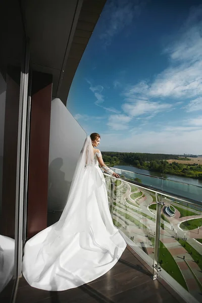 Красива брюнетка модель дівчина з вуаллю на голові в модному довгому весільному платті позує на балконі розкішного готелю — стокове фото