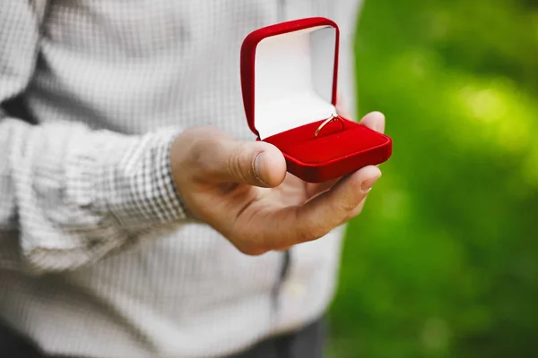 Rote Schachtel mit stilvollen goldenen Eheringen in den Händen des hübschen jungen Mannes, Heiratsantrag — Stockfoto