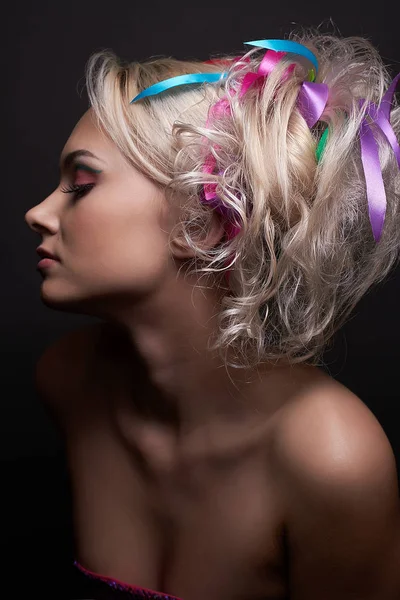 Beautiful blonde model girl with fashionable bright makeup and with colored ribbons in her stylish hairstyle, isolated at black background — Stock Photo, Image