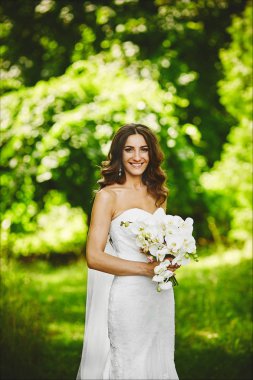 Elinde beyaz bir orkide ile şık bir gelinlik düğün saç modeli ile güzel esmer genç kadın doğada poz