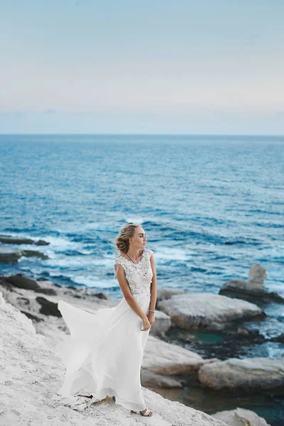 Giovane donna modello con corpo perfetto in elegante abito lungo bianco in posa sulle rocce sulla costa a Cipro — Foto Stock