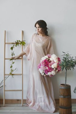 Baştan çıkarıcı tam dudaklar ve pembe ve beyaz çiçekler büyük bir buket tutan ve iç poz şık uzun bir elbise mavi gözlü güzel esmer model kadın