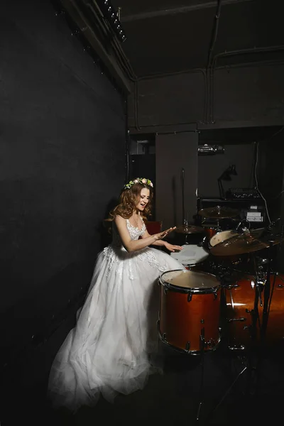 Hermosa mujer modelo joven con peinado de boda en un vestido de novia tocando en la batería — Foto de Stock