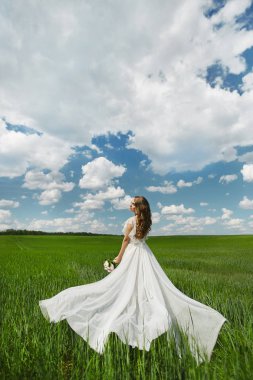 Yaz güneşli bir günde yeşil bir alanda poz beyaz uzun elbise düğün saç modeli ile güzel genç model kadın