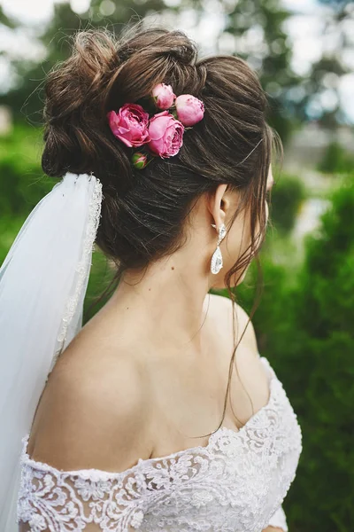 Mulher modelo bonita plus size com penteado de casamento elegante decorado com flores de rosa em um vestido de noiva elegante e em um véu posando ao ar livre — Fotografia de Stock