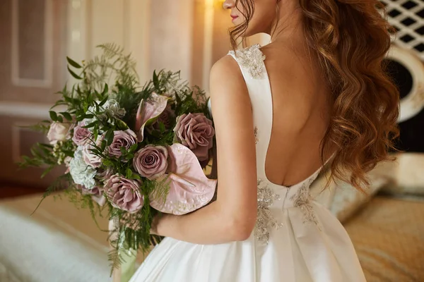 Beautiful and sexy brunette model girl in a fashionable wedding dress with a big luxury bouquet of flowers — Stock Photo, Image