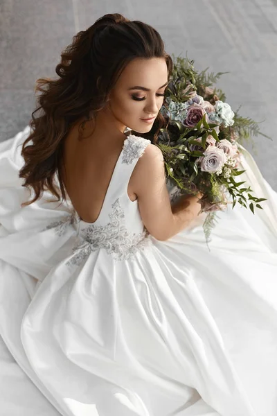 Menina modelo morena bonita e sexy em um vestido de noiva elegante com um grande buquê de luxo de flores — Fotografia de Stock