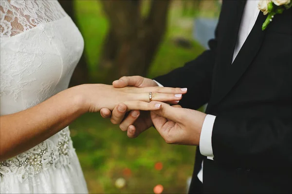 Der stilvolle Bräutigam zieht bei der Trauung den Verlobungsring am Finger seiner schönen Braut an. starke Männerhände und schöne Frauenhände mit Ehering und eleganter Maniküre — Stockfoto
