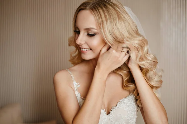 美丽和年轻的金发模特女人,与婚礼发型和专业明亮的化妆,调整她的耳环在内部 — 图库照片