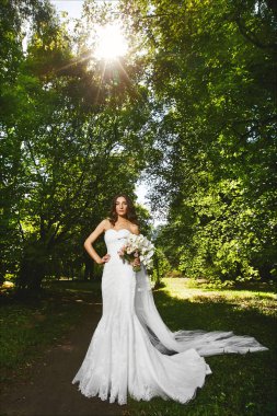 Seksi mükemmel bir vücut ile güzel ve şık esmer model kadın, beyaz şık gelinlik, gün batımında doğa çiçek bir buket ile poz