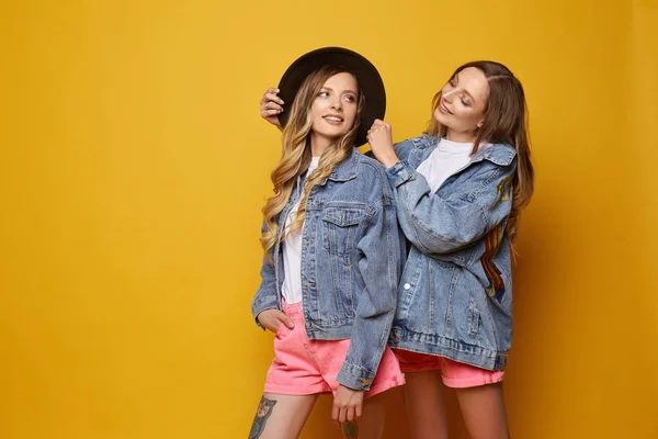 Två tvillingar bär jeans jackor på gul bakgrund — Stockfoto