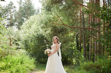 Parkta yürürken buket tutan lüks gelinlik güzel gelin