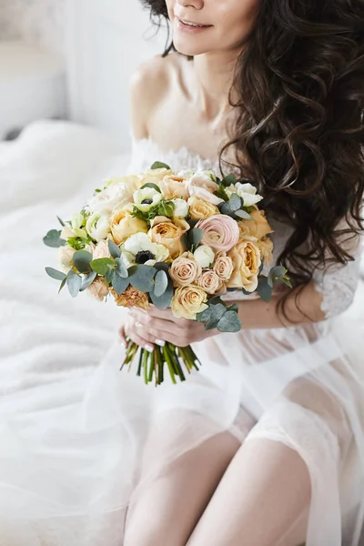 Tender bride with hairstyle sitting and keeping bouquet of fresh flowers — Stock Photo, Image