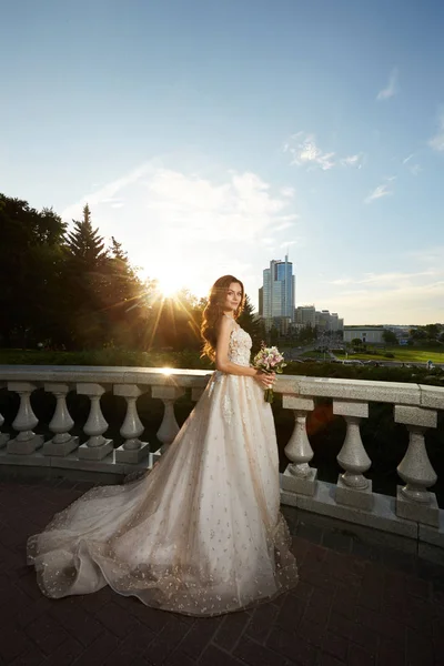 Uma noiva incrível em belo vestido de marfim posando ao ar livre no pôr do sol — Fotografia de Stock