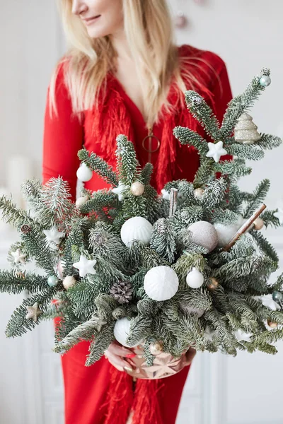 Ragazza modello alla moda in abito da sera rosso tenere in mano l'albero di Natale alternativo. Albero di Natale fatto in casa fatto di rami di abete con neve artificiale. Concetto di vacanze di anno nuovo — Foto Stock