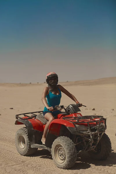 Sexy Model-Mädchen mit perfektem Körper und Bräune, mit Sonnenbrille und Helm, sitzt auf ATV und posiert in der Wüste — Stockfoto