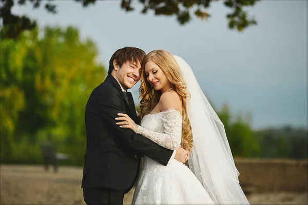 Счастливая пара только что вышла замуж, модная молодая блондинка в свадебном платье обнимает стильного красивого молодого человека в модном костюме. Счастливая пара влюбленных — стоковое фото