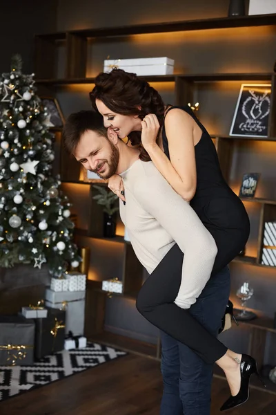 Beau couple qui s'amuse pendant la séance photo du nouvel an. Slim jeune femme en tenue modish et bel homme barbu, s'amusant et posant à l'intérieur près du sapin de Noël . — Photo