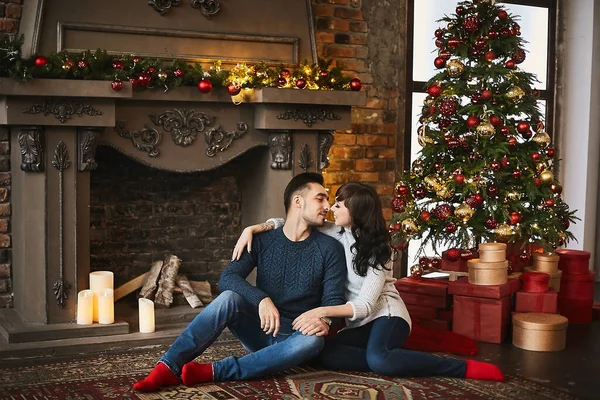 O jovem casal feliz, em camisolas quentes e meias vermelhas, abraçando e sentado no tapete autêntico perto da lareira e da árvore de Natal. Celebração de Natal e feriados de Ano Novo — Fotografia de Stock