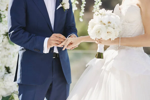 Mains avec des alliances. Mariage Modish mettant une bague dorée sur le doigt des mariées lors de la cérémonie de mariage. Couple aimant, une fille dans une robe de mariée et bel homme dans un costume bleu élégant — Photo